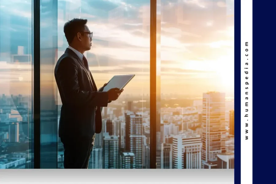 Business professional holding a tablet and overlooking a modern city skyline through tall glass windows at sunset — symbolizing leadership, strategy, and insights from a Bali Business Guide.